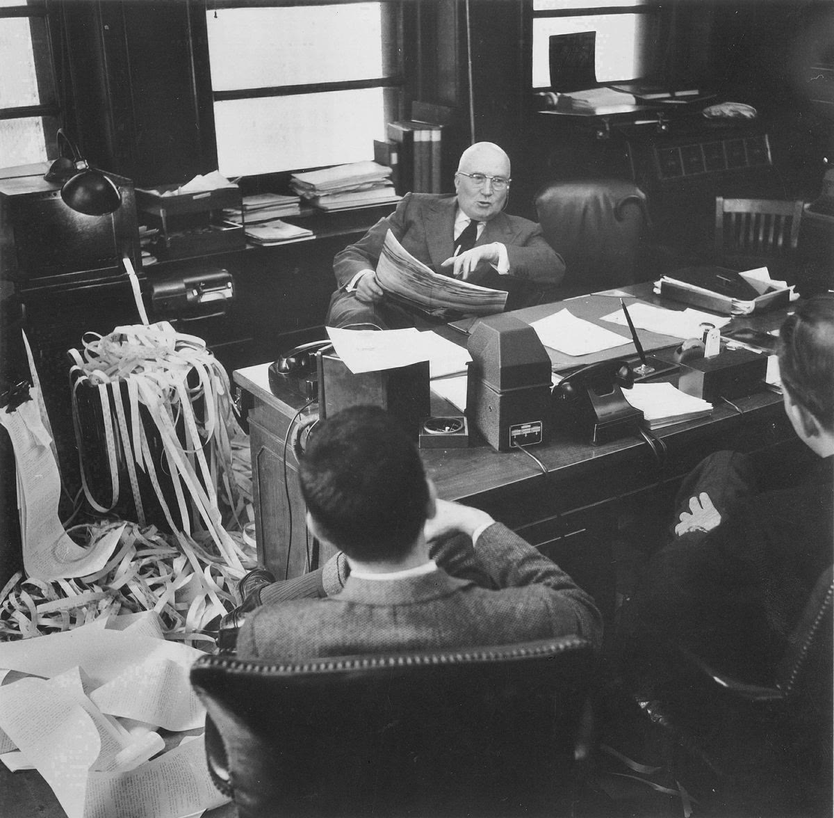Gerald Loeb tại bàn làm việc trên phố Wall, xung quanh là giấy tờ và băng ticker